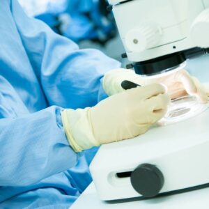 A laboratory technician in protective gear examining a petri dish under a microscope, representing meticulous scientific investigation.