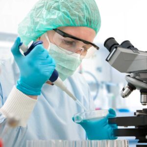 A biomedical scientist pipetting a sample into a petri dish under the scrutiny of a microscope, illustrating the precision of pharmaceutical research.