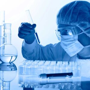 A lab technician in full protective gear handling a test tube with blue liquid, set against a backdrop of laboratory glassware, embodying the careful process of scientific experimentation.