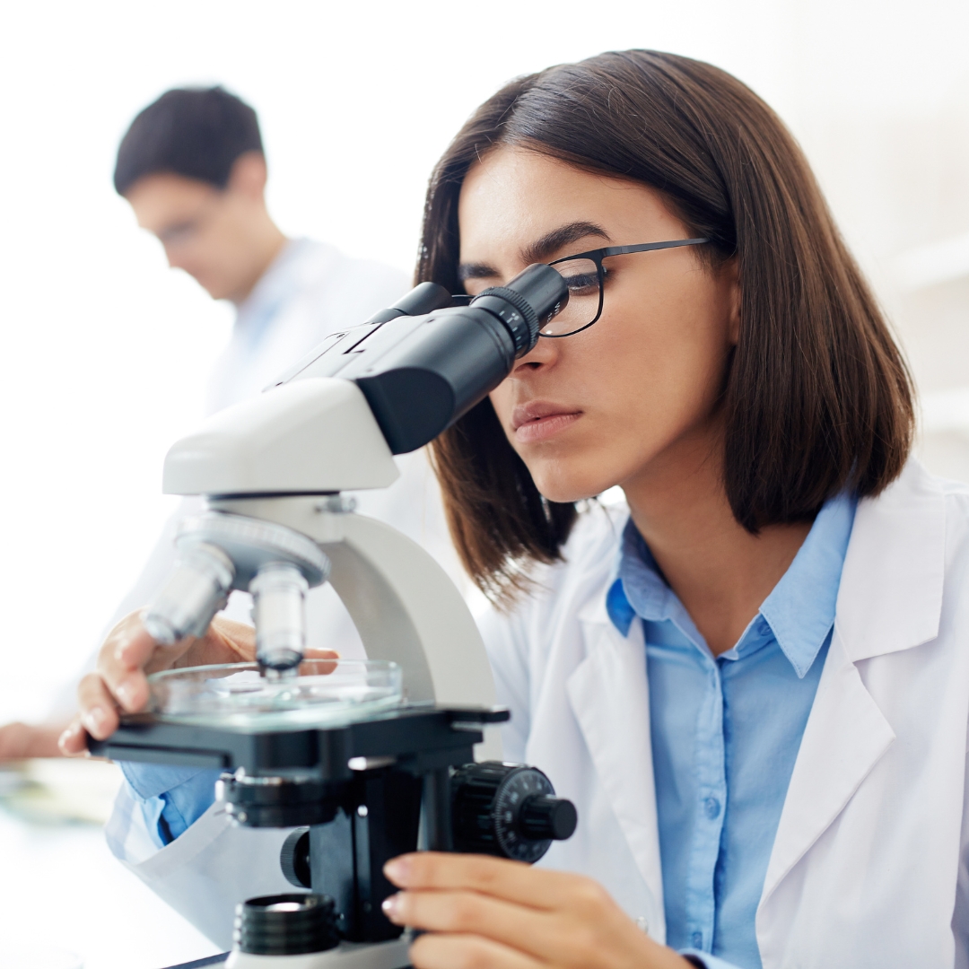 A female scientist intently using a microscope in a laboratory setting, indicative of medical or biological research.